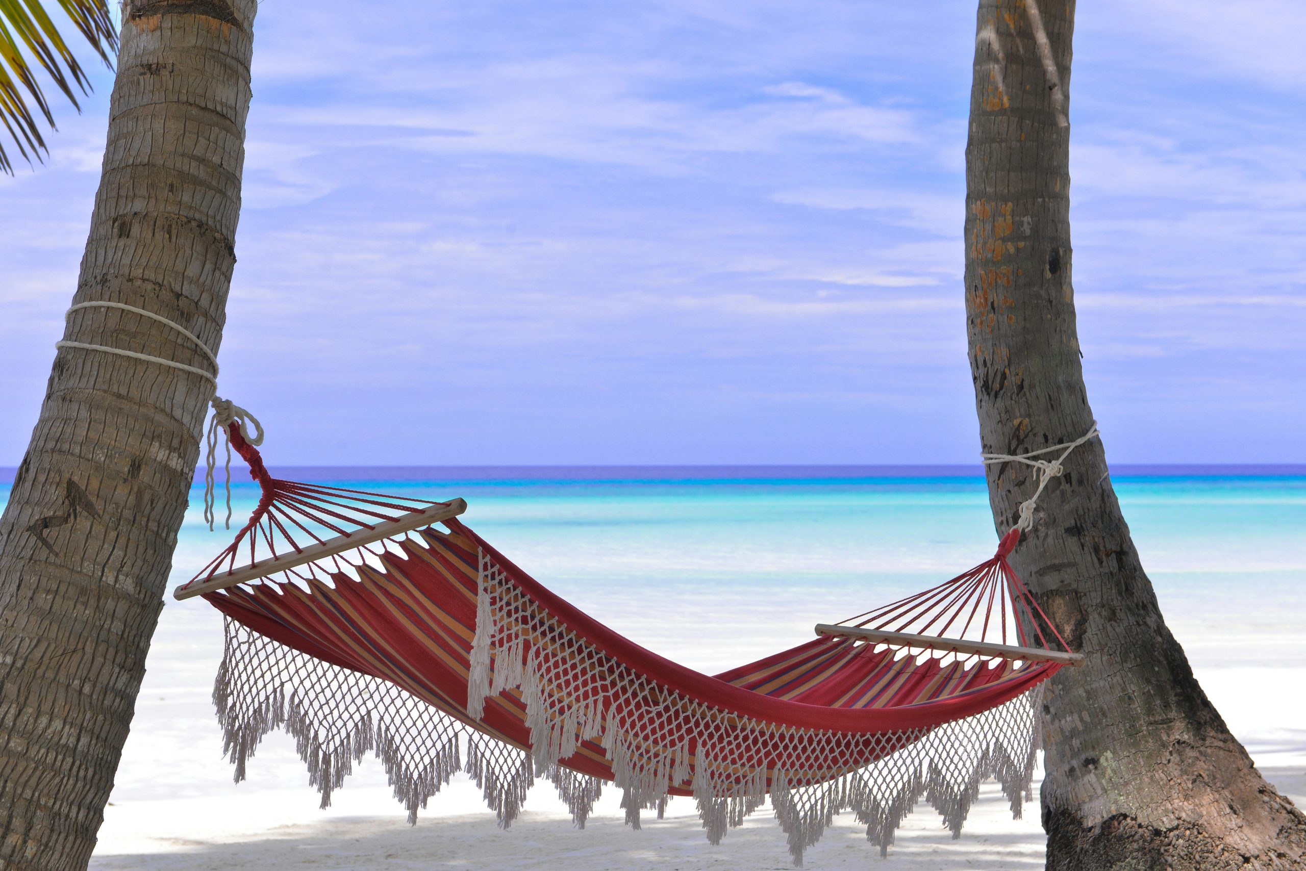 Hamaca roja entre palmeras frente al mar turquesa del Caribe, símbolo del estilo de vida relajado que buscan los extranjeros al invertir en bienes raíces en la región.
